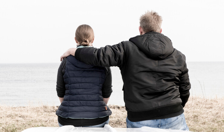 Et par sidder med afstand til hinanden ved stranden