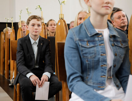 To konfirmander sidder på deres særlige pladser i kirken under en konfirmation.