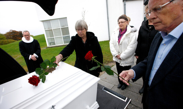 Pårørende i sorg tager afsked ved kisten, inden rustvognen kører kisten væk.